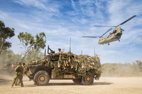 A Bushmaster Protected Mobility Vehicle prepares to depart the landing zone as a CH-47F Chinook takes off.