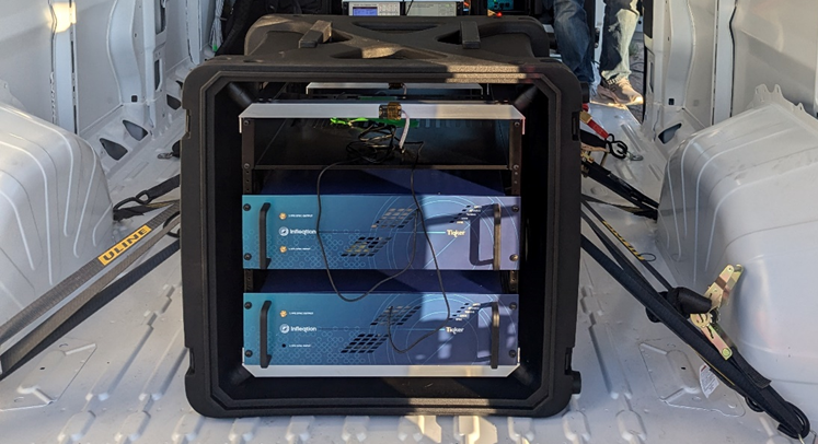This coloured photograph shows a rack of equipment in a cubic hardened case, secured to the inside of a vehicle with ratchet straps.