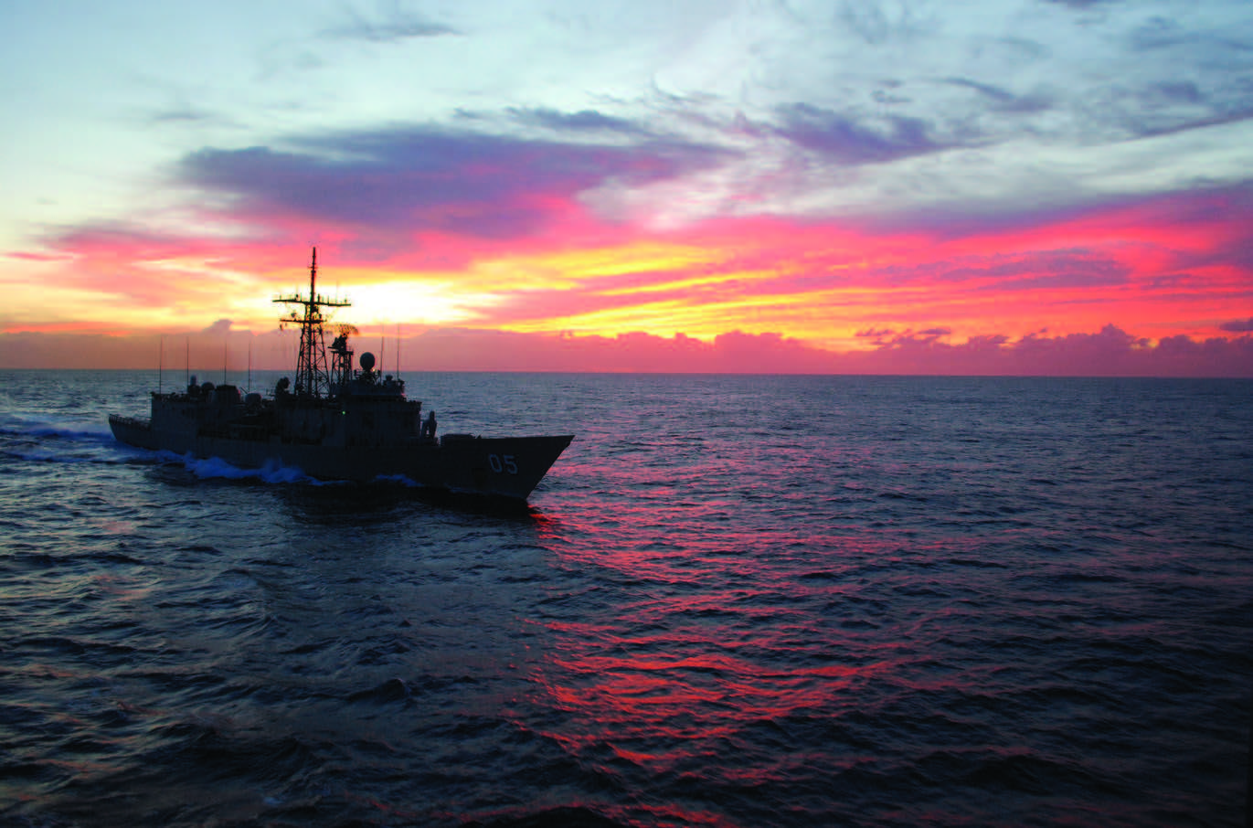 Naval Ship sailing with the sunset behind it.