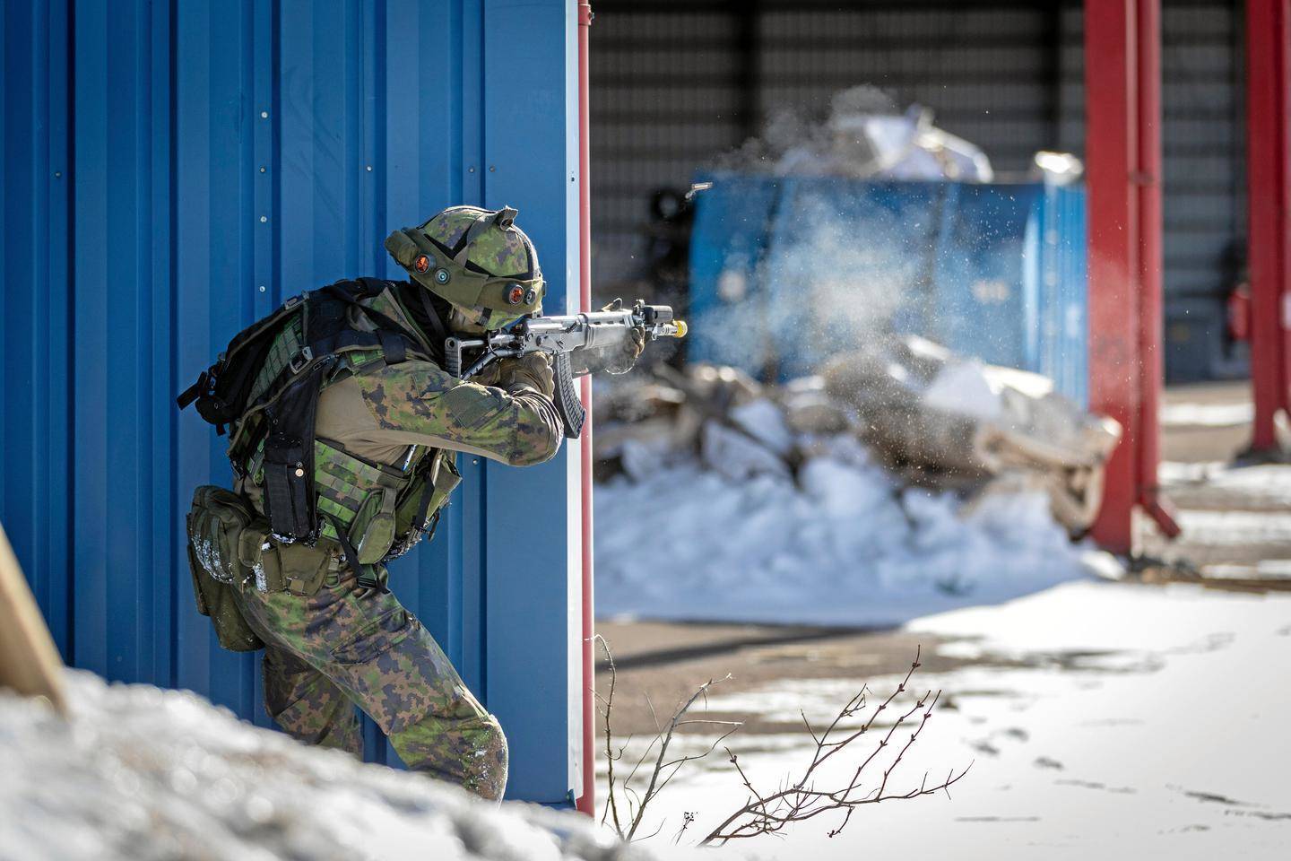 An armed soldier firing a rifle from behind a wall in a snowy building setting.