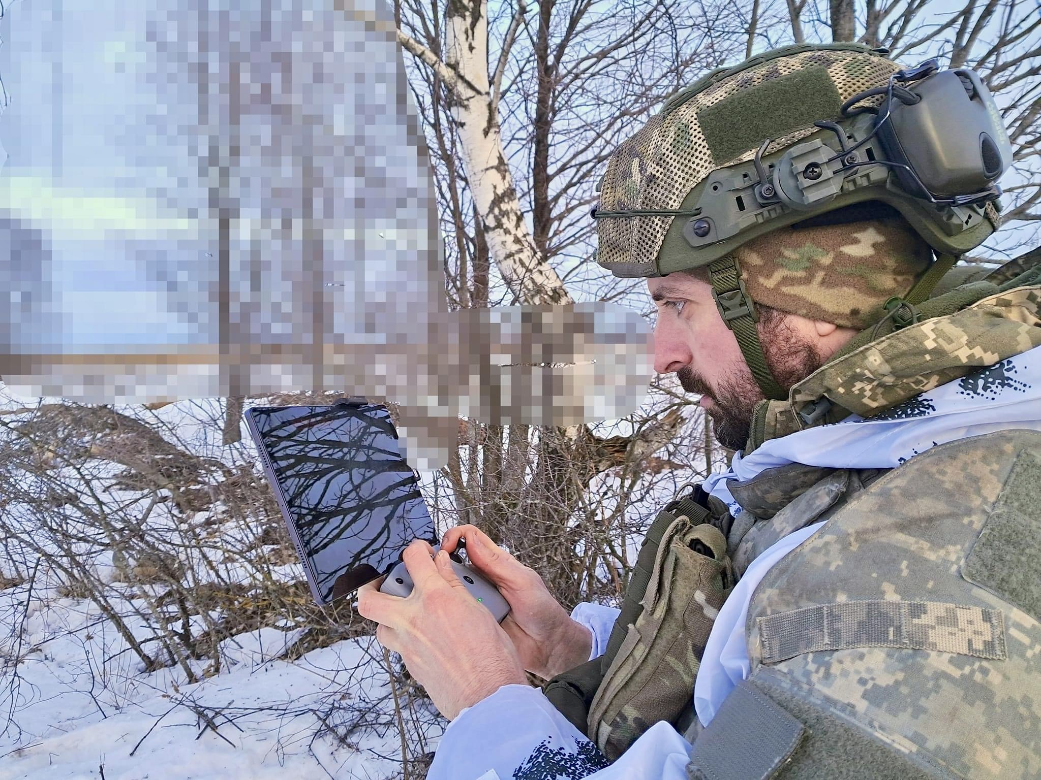 Soldier in a lightly wooded area operating a tablet screen and drone controller.