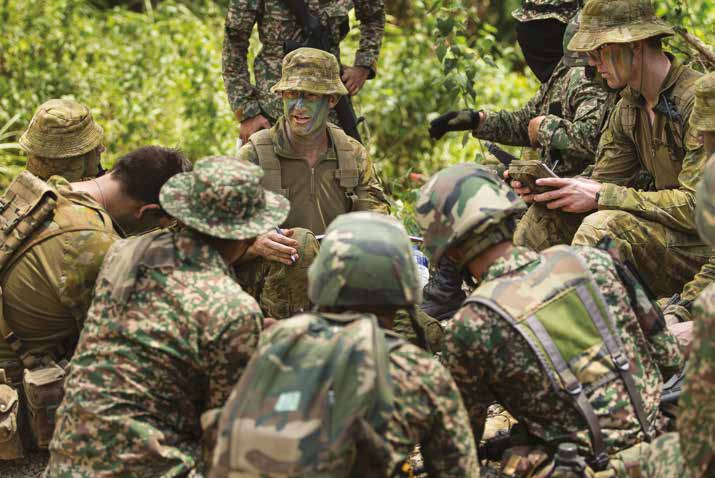 Soldiers from Australia and Malaysia kneel around a mud map to briefed in the field.