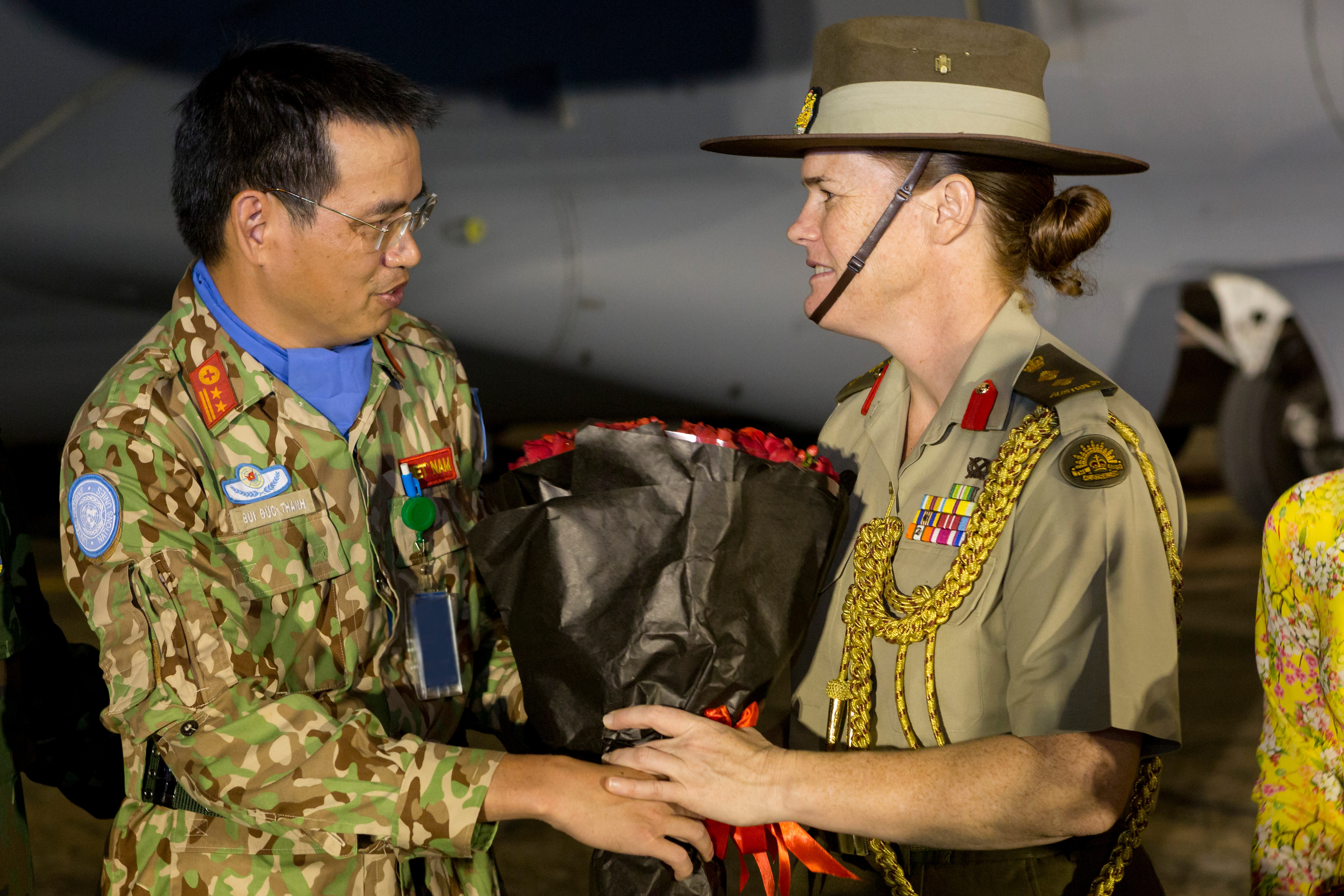 Vietnam People's Army medical officer, Lieutenant Colonel Bui Duc Thanh presents Australia's Defence Attache - Hanoi, Colonel Nerolie McDonald with flowers during the welcome home ceremony for the Vietnamese medical contingent following their deployment to South Sudan in 2019 in Ho Chi Minh City, Vietnam. Both the officers are wearing uniforms. Australia supported Vietnam's deployment of a Role 2 field hospital with two airlift tasks from Vietnam to South Sudan and return.