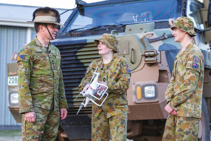 A Male officer talking with 2 Female soldiers while they hold an off the shelf drone.