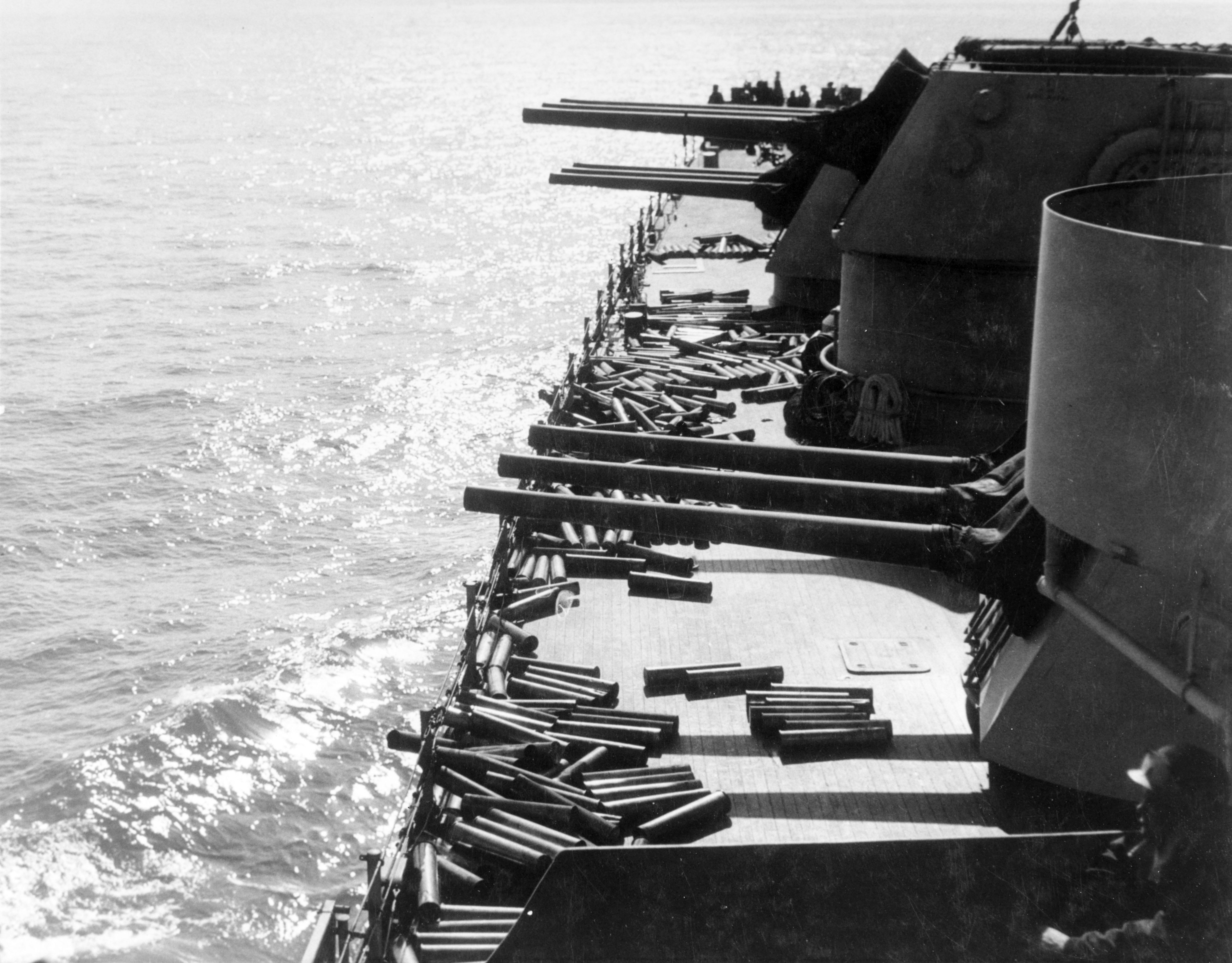 The forward three triple 6-inch gun turrets of the US Navy cruiser USS Brooklyn are shown in the image. The Brooklyn is providing providing Naval Gunfire Support to troops ashore during the initial Operation Husky landings. The turrets are traversed to port. Scattered on the decks are expended brass cartridge cases ejected from the gun turrets.