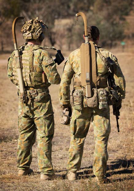 2 soldiers standing in the field with back harnesses that the holds the weight of their weapons.