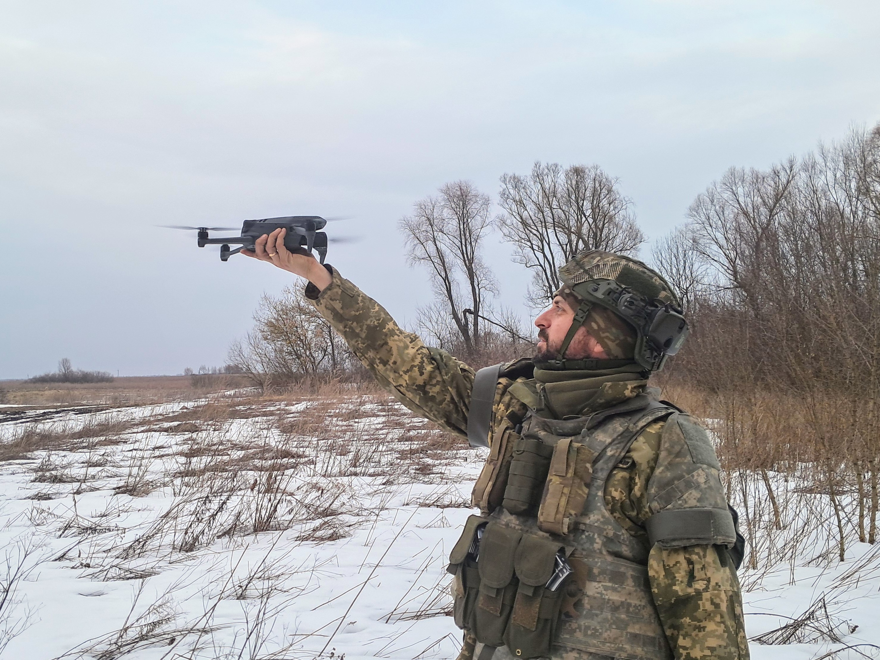 Soldier on snow laden ground holding a drone in front and above head height.