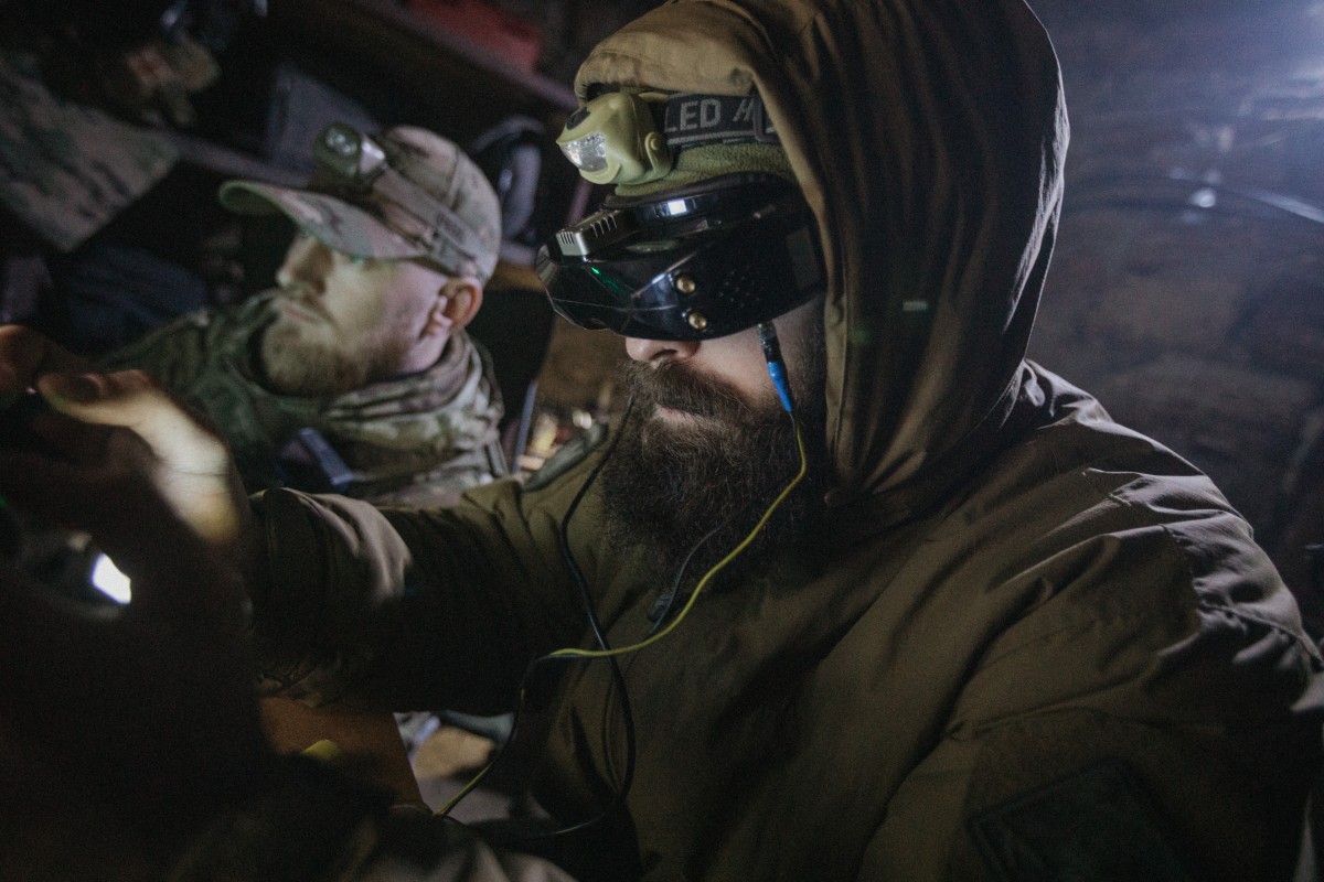 Two soldiers at night, both looking forward to the left of the image, the nearest soldier has goggles on, presumably operating a drone in FPV, the rear soldier in image is observing.