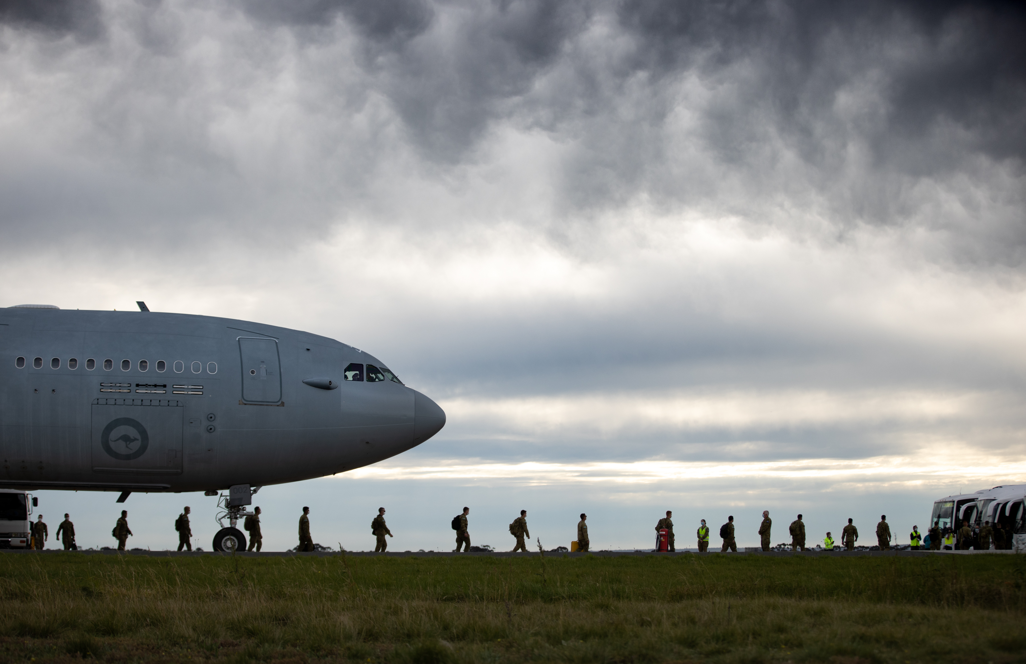 Nose of military transport aircraft from left with troops along ground walking away from the aircraft in single file