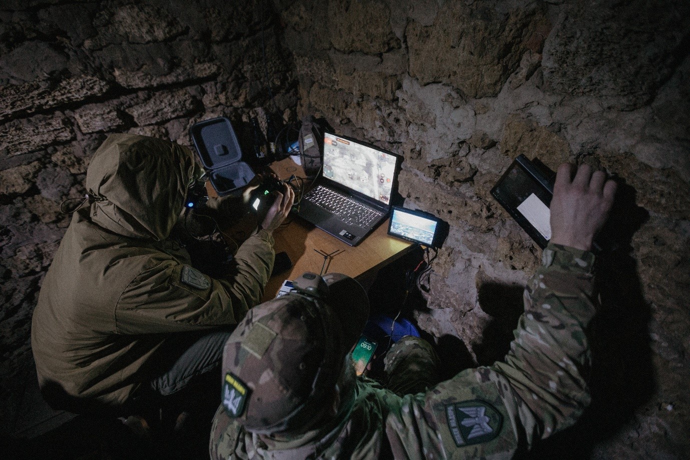 A team of Ukrainian drone operators performs a mission in the corner of a dimly lit brick walled room.