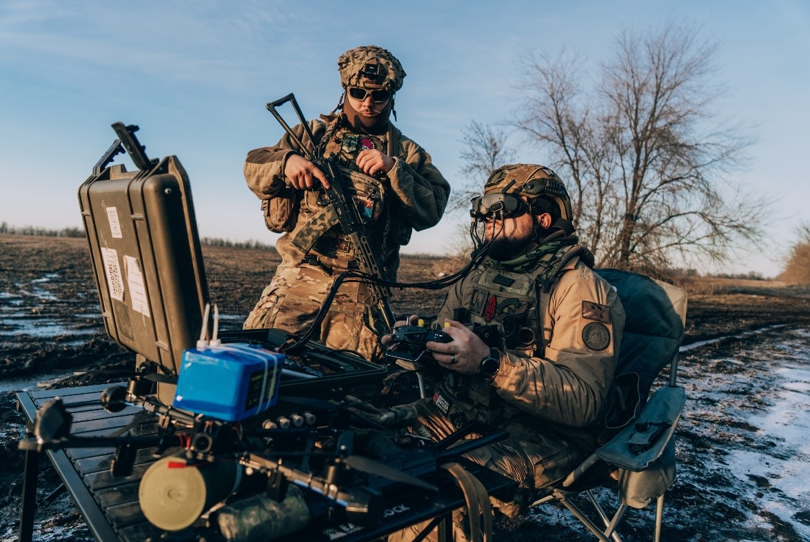 Military drone operators’ training at a table and chair in a snowy field.