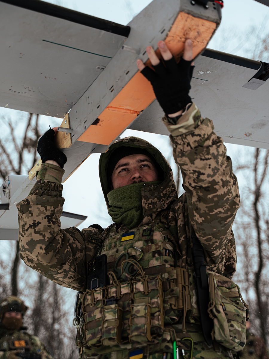 Pre-flight preparations being performed by a drone operator holding a fixed wing air vehicle above and inspecting the underside.