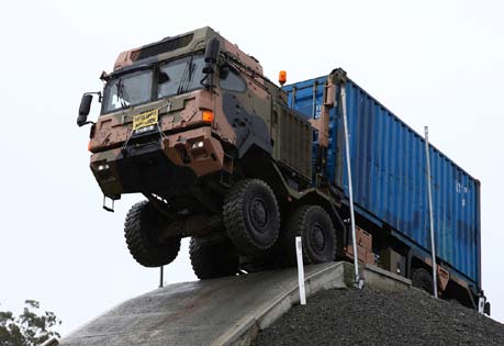 A driver under instruction negotiates the Greenbank Driver Training Area course to prepare him for logistics tasks on the Rheinmetall MAN truck, seen here carrying an ISO container.