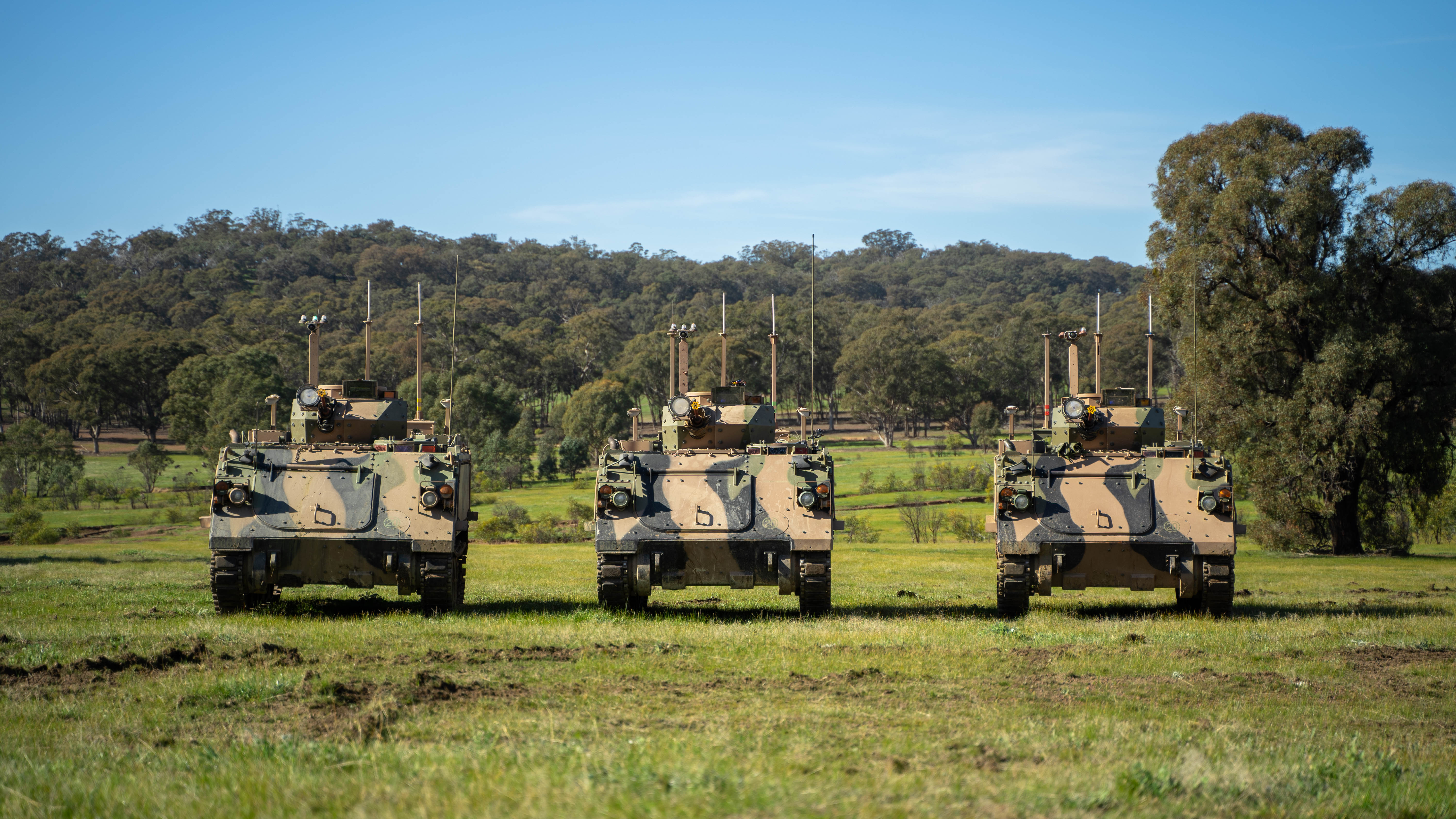 Three Australian Army M113AS4 Armoured Personal Carriers enhanced as Optionally Crewed Combat Vehicles (OCCV) stand ready to demonstrate their potential at Puckapunyal Army Base.