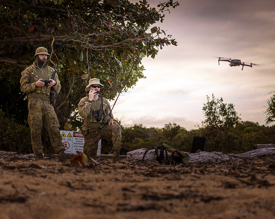 Two army soldiers in bushland operating a small UAV.