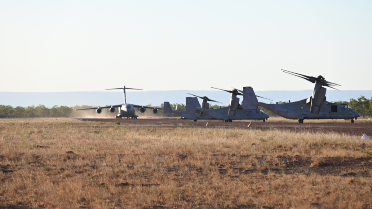 Royal Australian Air Force Boeing C-17A Globemaster III prepares for takeoff at Nackaroo Airfield, Bradshaw Field Training Area near three United States Marine Corps MV-22B tilt rotor aircraft as part of Exercise Loobye.