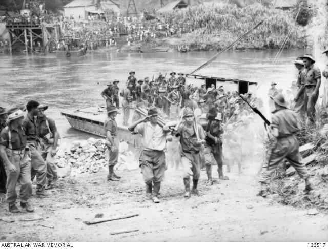 Japanese soldiers salute Australians of the 24th Brigade as they disembark from a punt crossing the Padas River and march to a prisoner of war compound at Beaufort, British North Borneo, on 18 Sep 1945