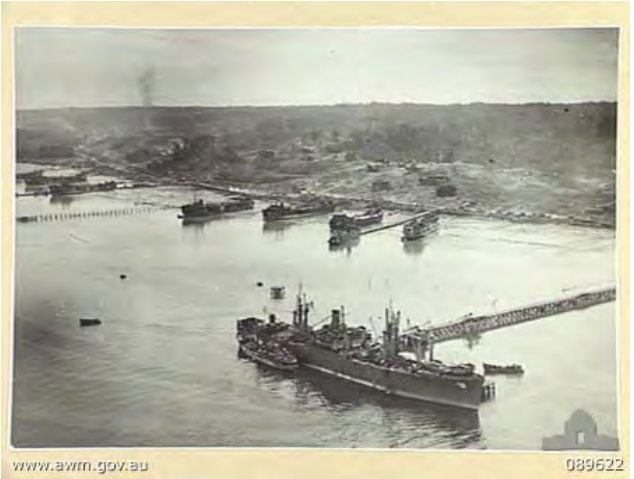 USS Titania docks at the South Wharf at Tarakan while LSTs are beached in the background.