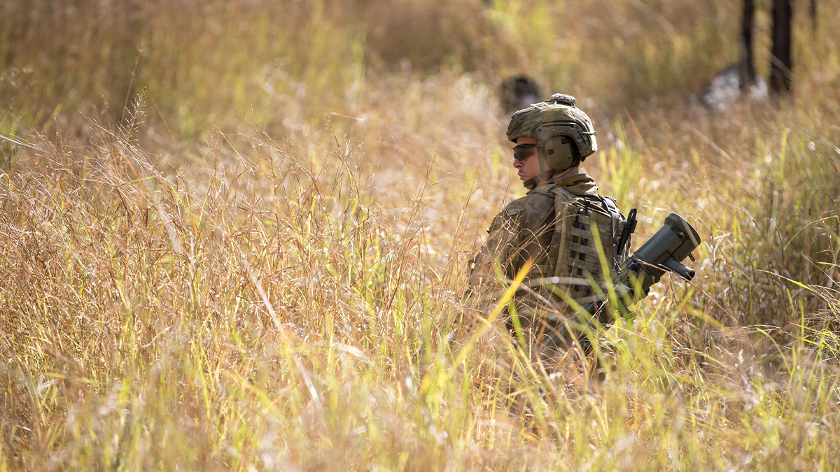 A soldier from the 6th Battalion, Royal Australian Regiment, patrols through tall grass while carrying an 84mm Carl Gustaf recoilless rifle at Shoalwater Bay Training Area, Queensland.