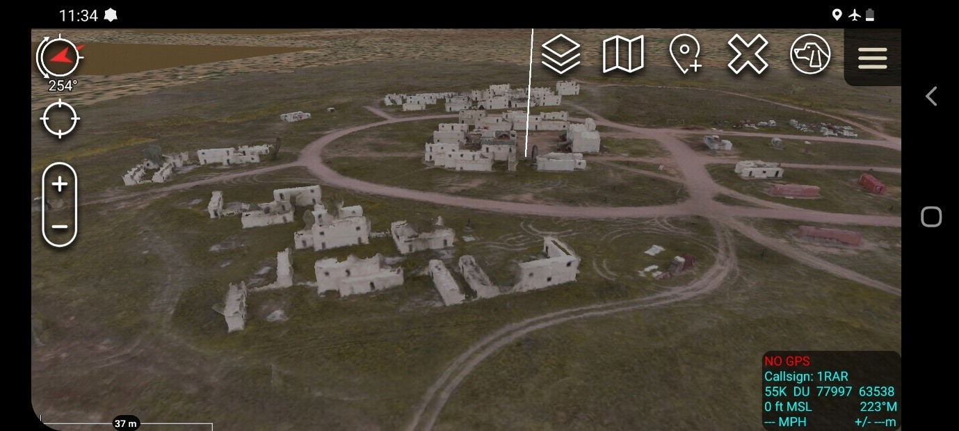 This coloured screen capture depicts a three dimensional rendered image of the ruins of a village and dirt roads in the desert. The screen capture also shows directional tools and map layers, and text in the bottom right corner depicting the user’s Unit information.