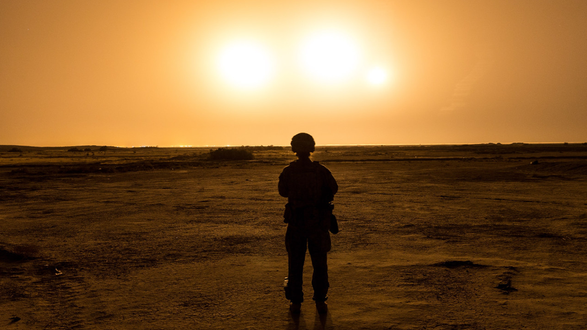 An illuminated mortar round at night and soldier silhouette