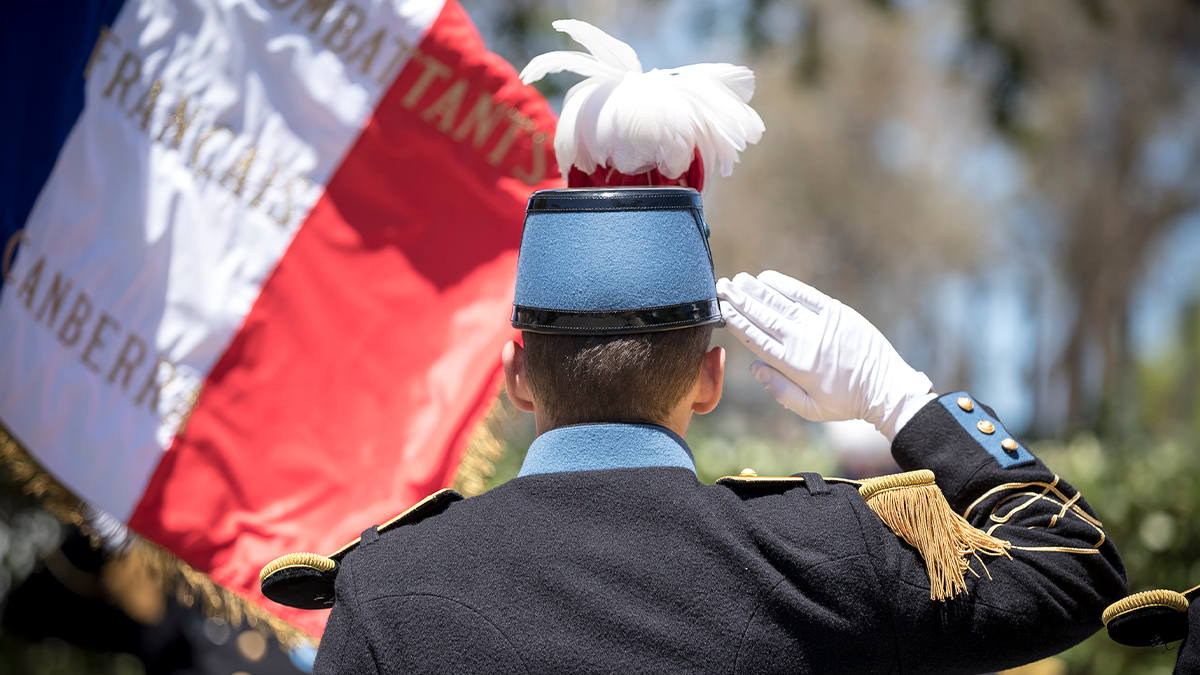 French Military member from behind saluting with a French coloured flag in the background