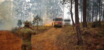 An Australian Army soldier from 25/49 Royal Queensland Regiment watches the backburn operations as he awaits clearance and escorts through an active fire zone for delivery and setup of two bouywalls.