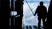 Soldier silhouette on rear ramp of aircraft with clouds in background