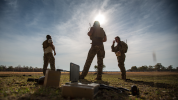 Three soldiers on a field with sun shining behind them