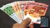 A handful of 100 to 10 Euro denomination notes fanned out in a hand with the cover of Spotlight Brief 7/21 in the foreground lower right corner