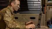 Soldier with face paint sitting at a laptop in a workshop environment