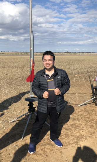 Khuong Nguyen standing in front a rocket on a launch stand in a field.