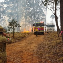 An Australian Army soldier from 25/49 Royal Queensland Regiment watches the backburn operations as he awaits clearance and escorts through an active fire zone for delivery and setup of two bouywalls.