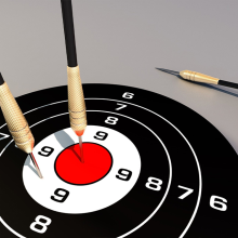 Two darts in a dartboard and one beside the dartboard