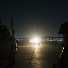 Soldier in foreground with night vision and aircraft in background with lights glaring