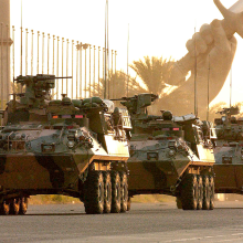 Three APCs driving towards us on a road with Iraq's Victory Arch in the background