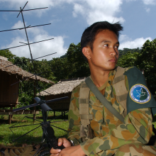 Soldier holding an antenna with straw roof huts in background
