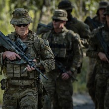 Armed soldiers walking with blurred scrub in the background