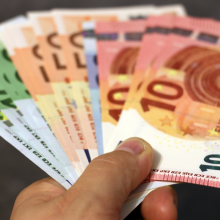 A handful of 100 to 10 Euro denomination notes fanned out in a hand with the cover of Spotlight Brief 7/21 in the foreground lower right corner