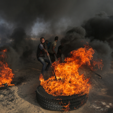 A burning tyre in Gaza, with a man placing a pole inside the burning tyre