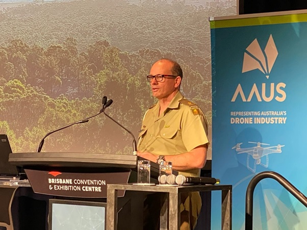 MAJ Charles Eling behind a lectern, labelled Brisbane Convention Centre, with a AAUS banner in the background.